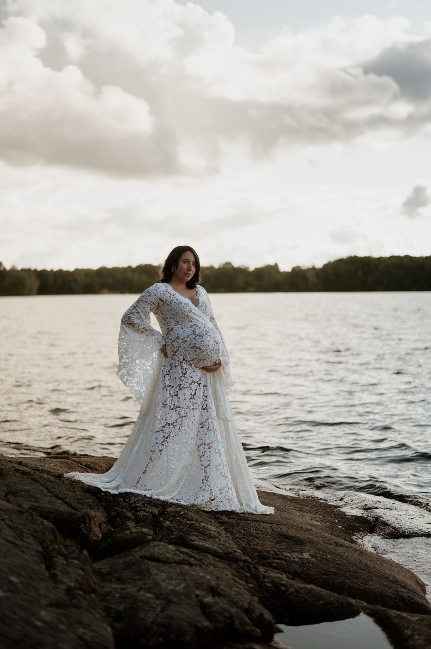 Gravid kvinna står på klipporna i solnedgången.