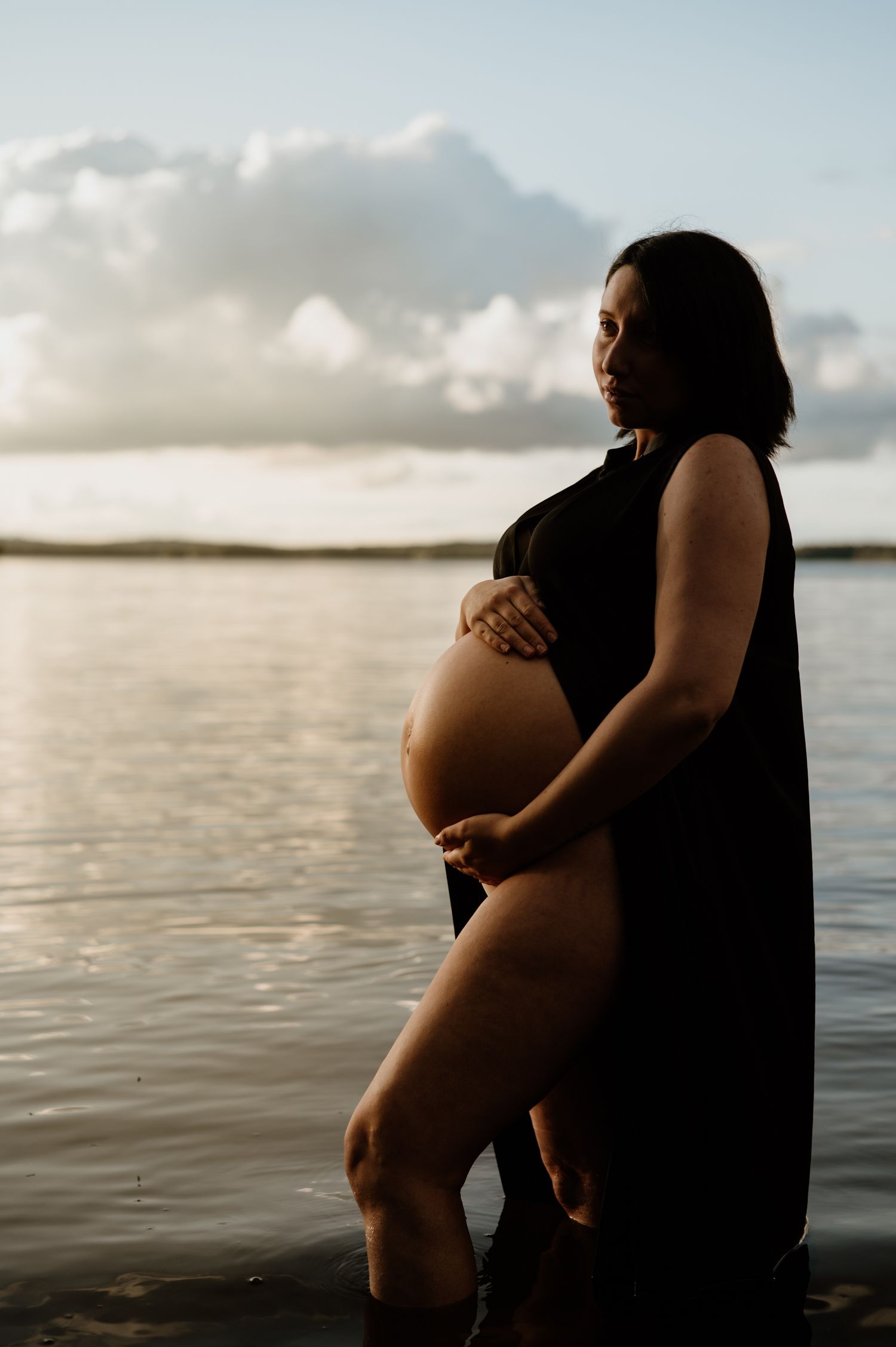 Gravid kvinna står i vattnet i solnedgången.