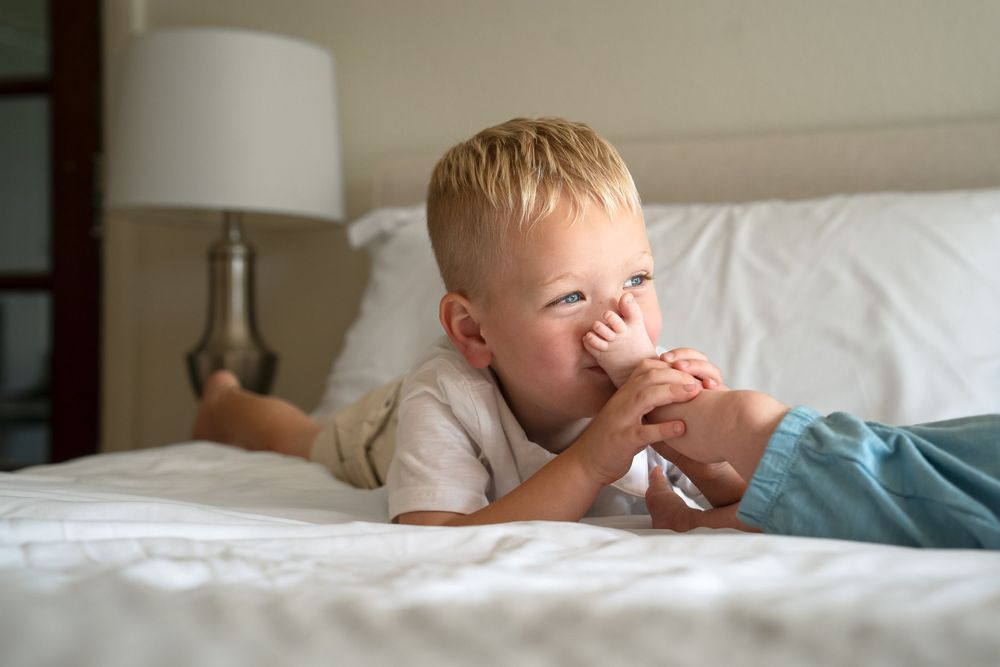 In home portrait session San Antonio Texas toddler boy holding newborn baby sister's foot