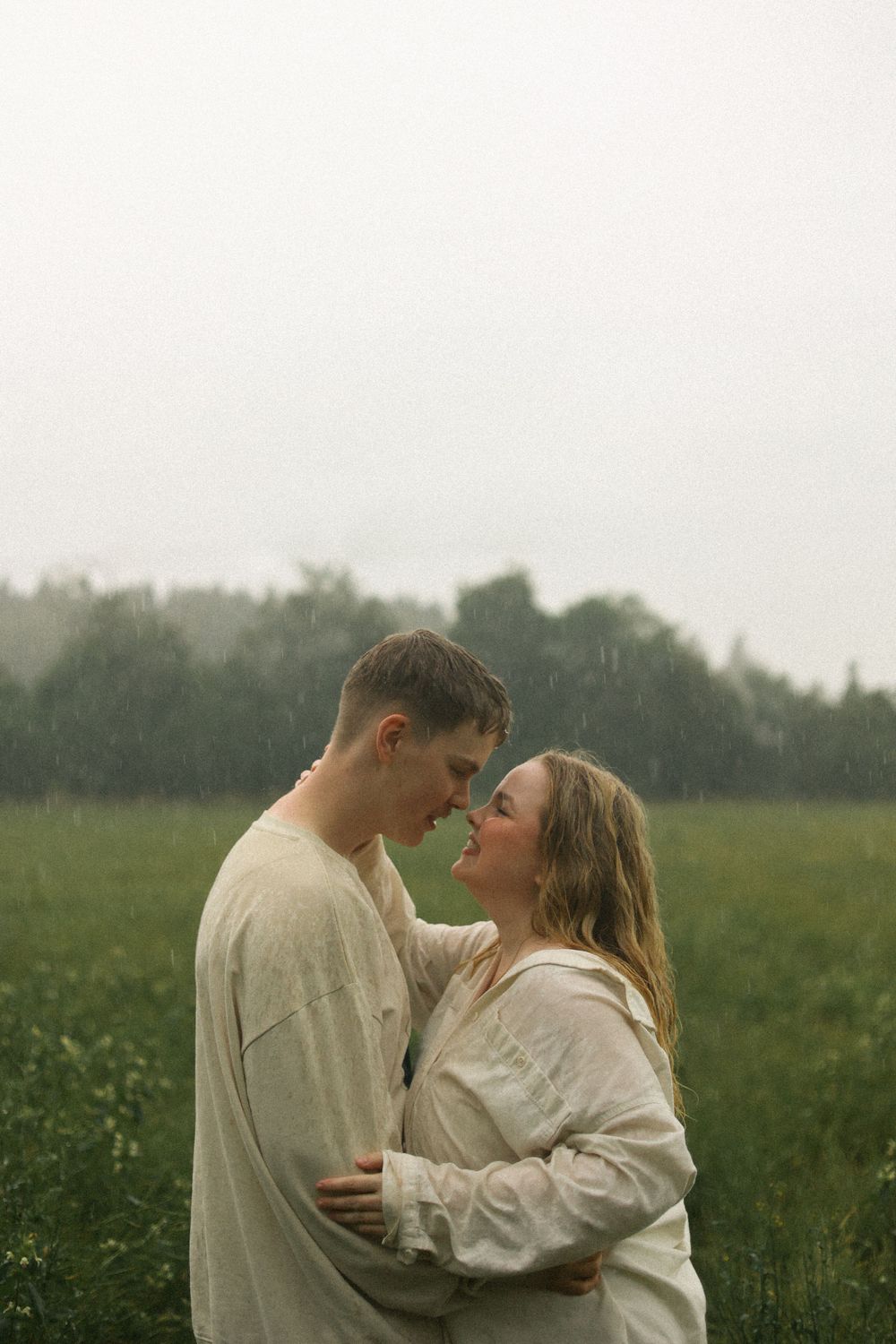 Intimate portrait of couple in matching cream sweaters embracing in a foggy meadow.