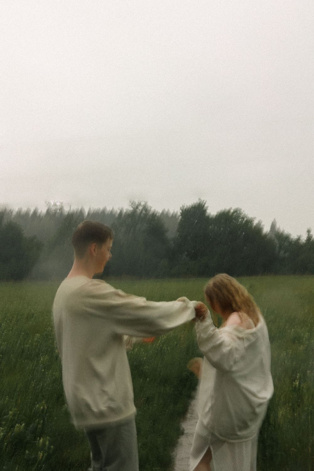 Couple in casual outfits sharing a playful moment in a misty field.