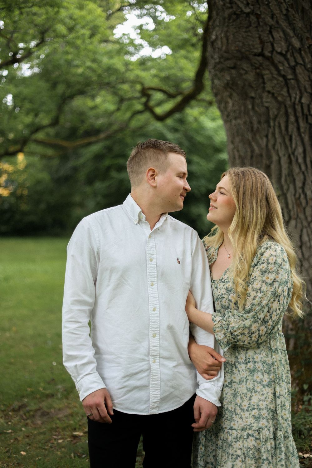 A couple shares an intimate moment under a large tree in a green summer setting.