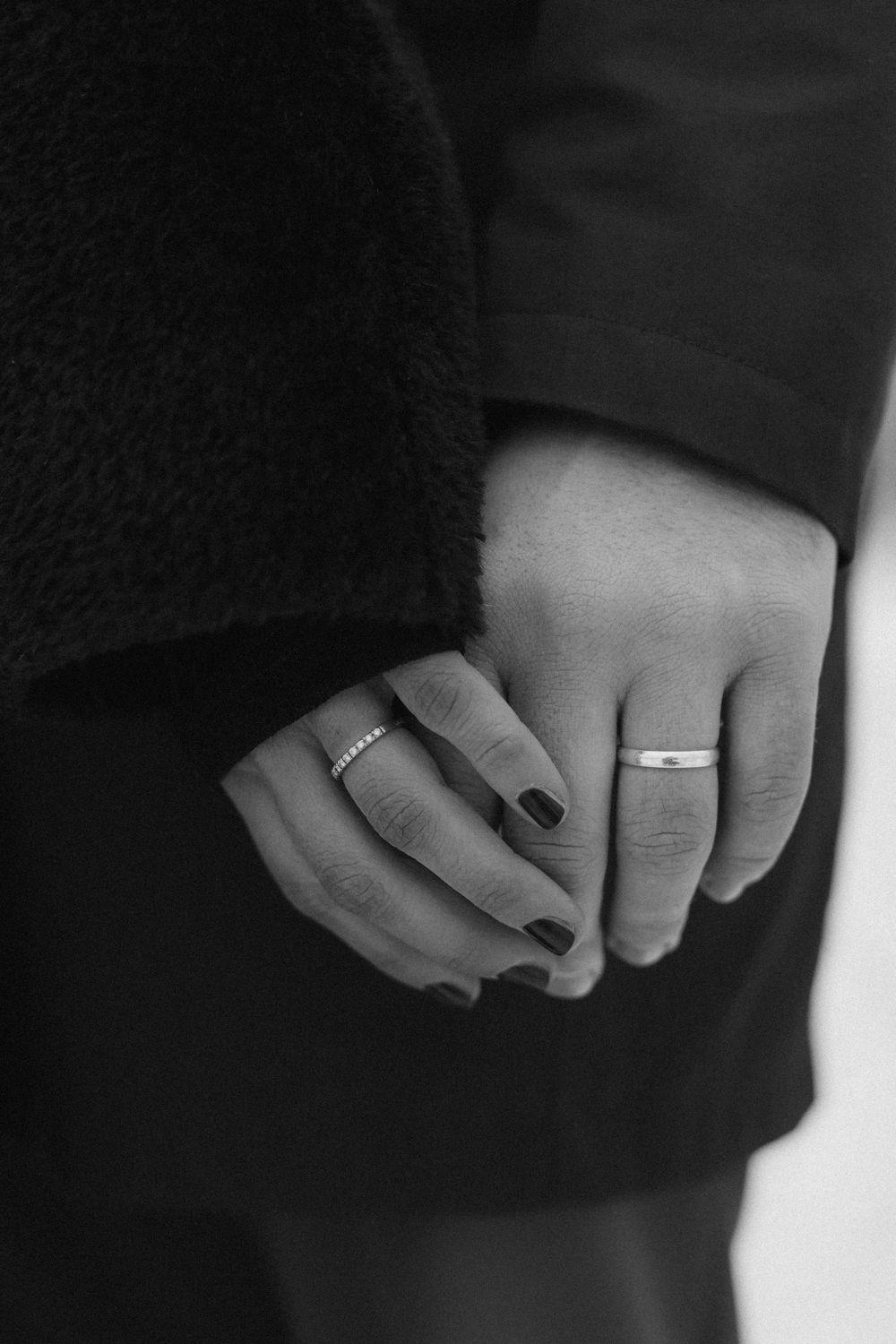Close-up black and white photo of two hands with wedding rings clasped together.