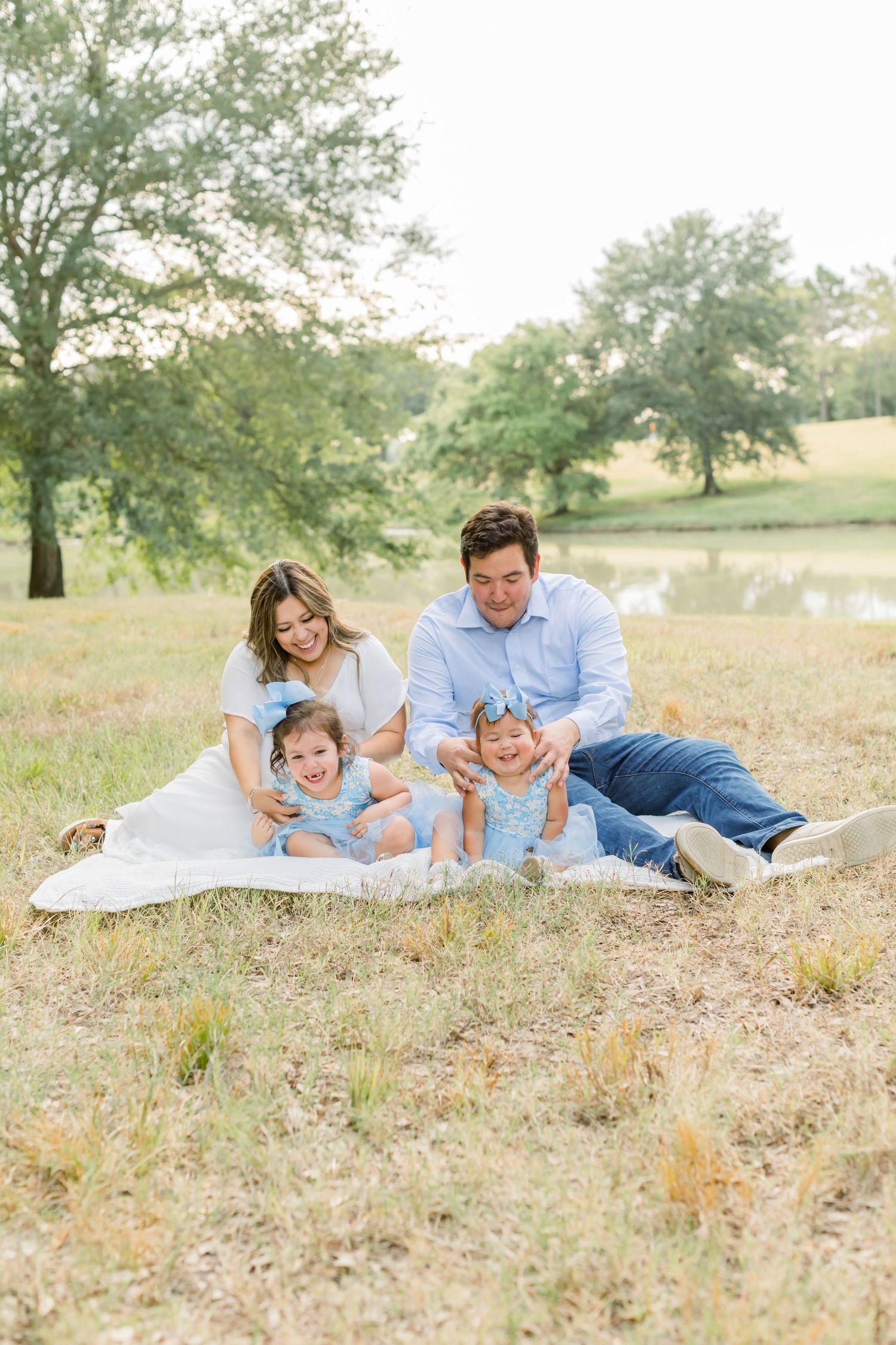 Joyful family moment on white blanket in sunny field with pond view.