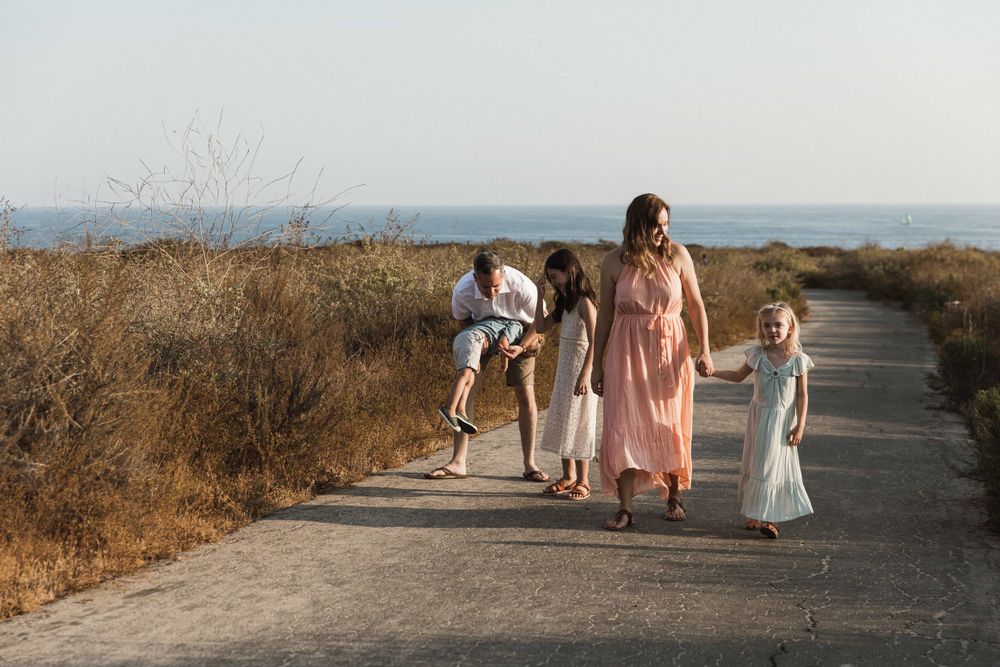 Family with three children walking on a coastal path surrounded by golden dry grass and ocean views.