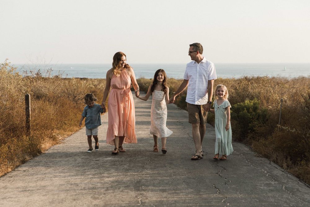 Happy family of five holding hands walking on a scenic coastal path at golden hour.