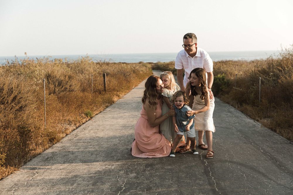 Loving family of five gathered together on a coastal path smiling and playing outdoors.