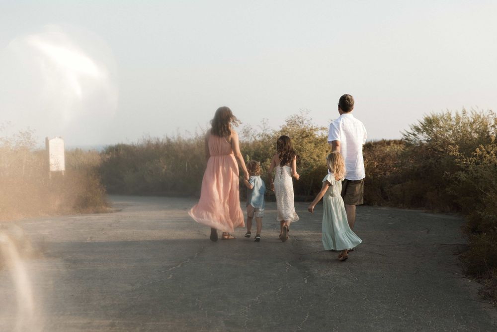 Family of five walking away down a misty coastal path holding hands at sunset.