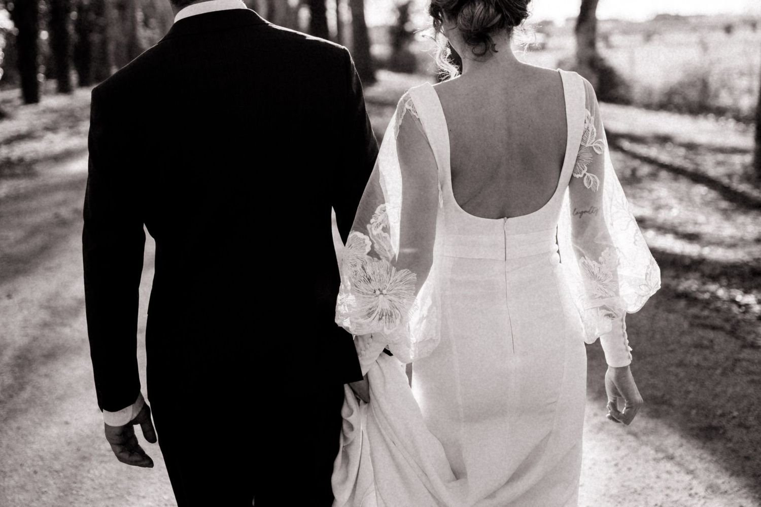 Bride and groom walking together on a tree-lined path in black and white.
