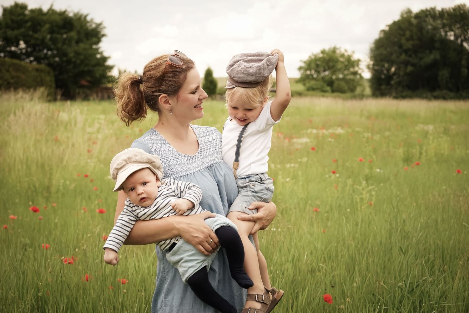 Mama mit ihren 2 Söhnen im Arm auf einer Wiese mit rotem Mohn während einer natürlichen Familienfotosession Outdoor Wien