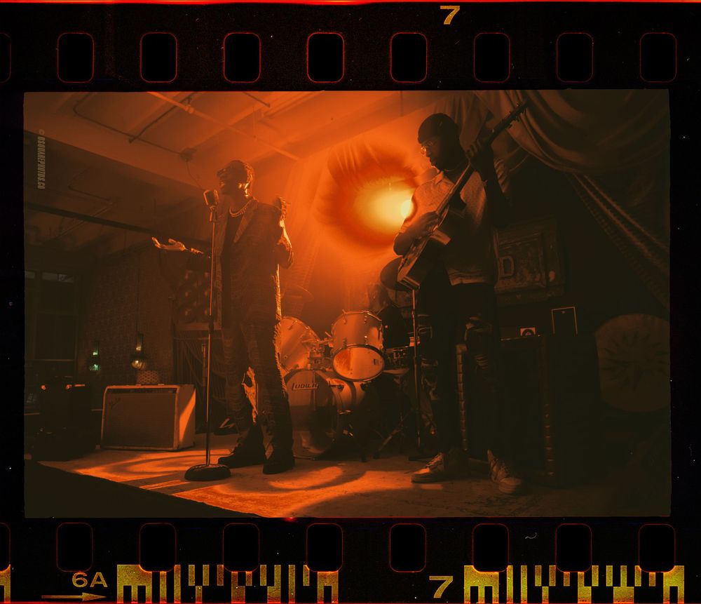 Musicians perform on stage bathed in dramatic orange lighting and atmospheric smoke effects.