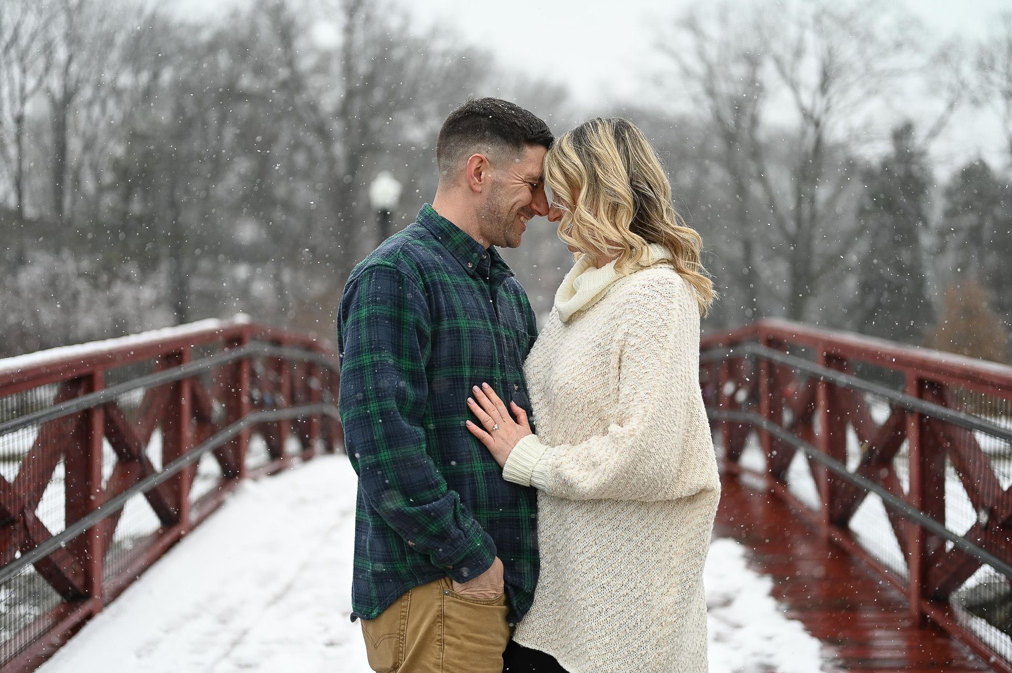 Couple walking together on a snowy red wooden bridge in winter.