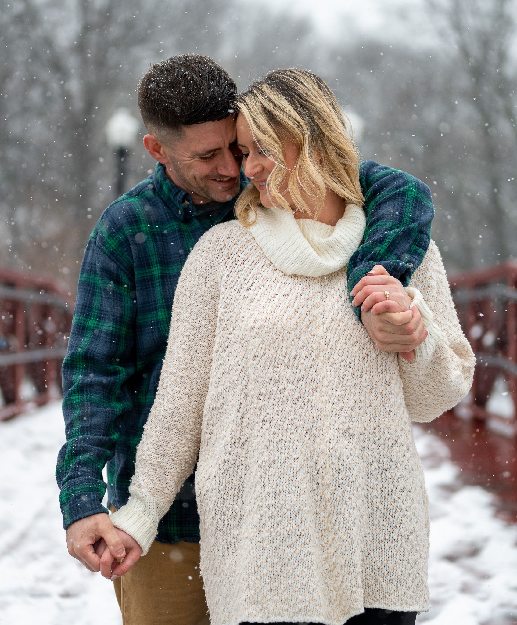 Couple in winter clothing embracing on a snowy bridge.