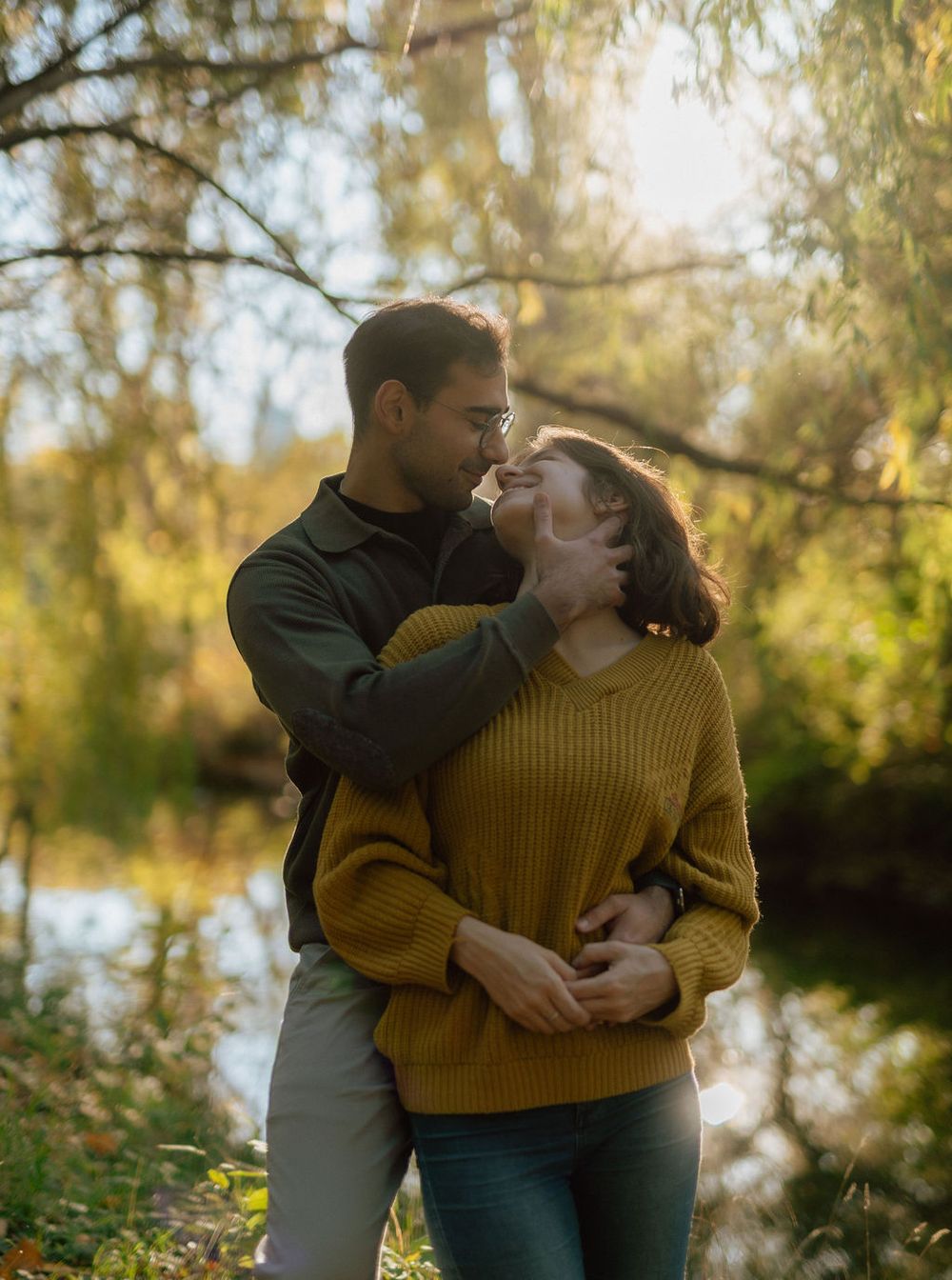 Loving couple embracing outdoors wearing autumn sweaters near a pond.