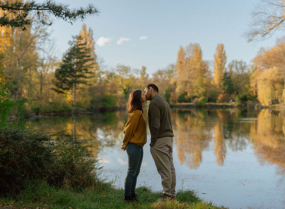Couple sharing romantic moment by lake with fall foliage reflections.
