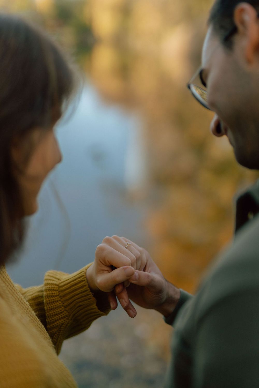 Close up of hands touching during intimate moment by autumn lake.