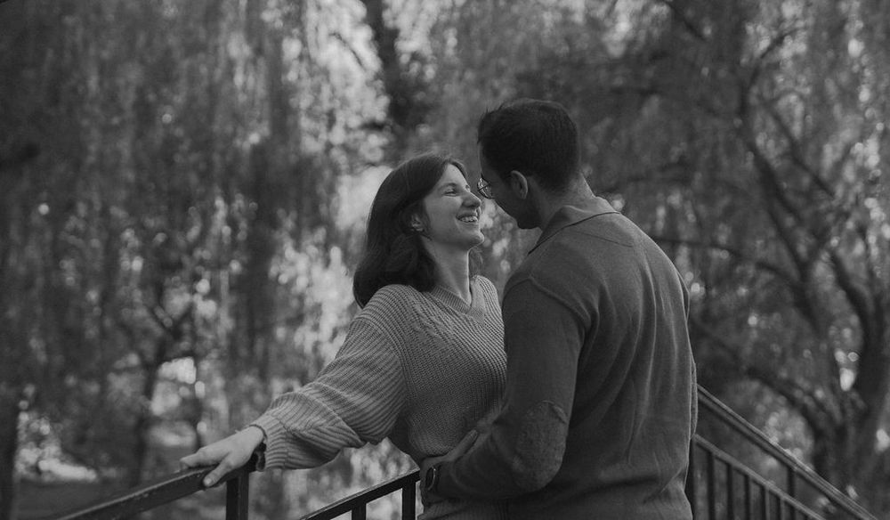 Romantic couple sharing an intimate moment on a bridge in black and white.
