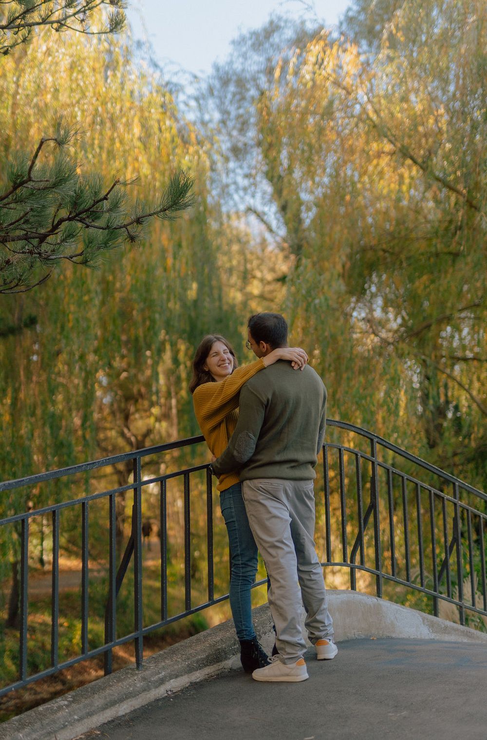 Couple embracing on a bridge with golden autumn willows in the background.