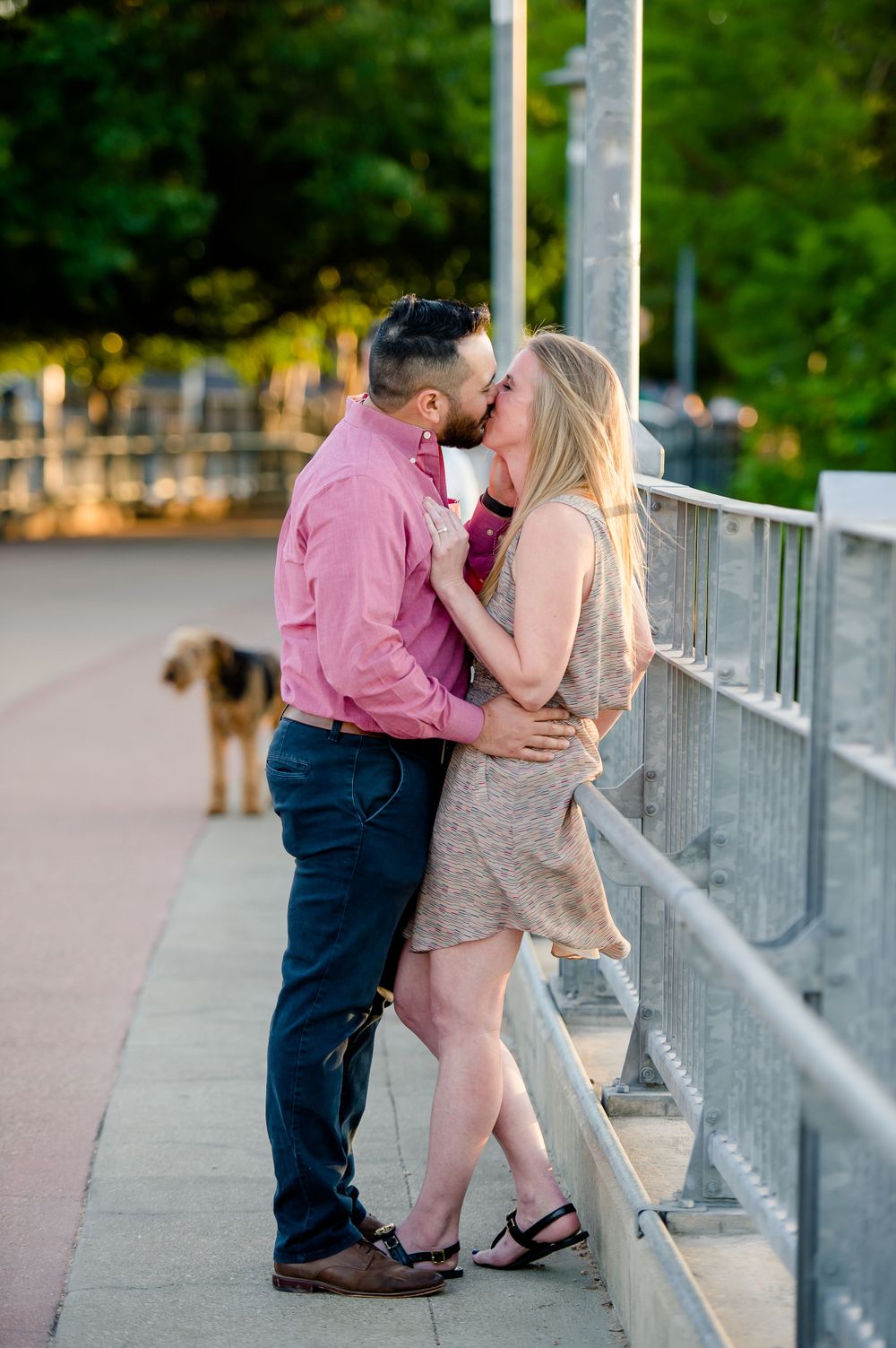 Romantic engagement photo on bridge with couple in pink and beige at sunset.