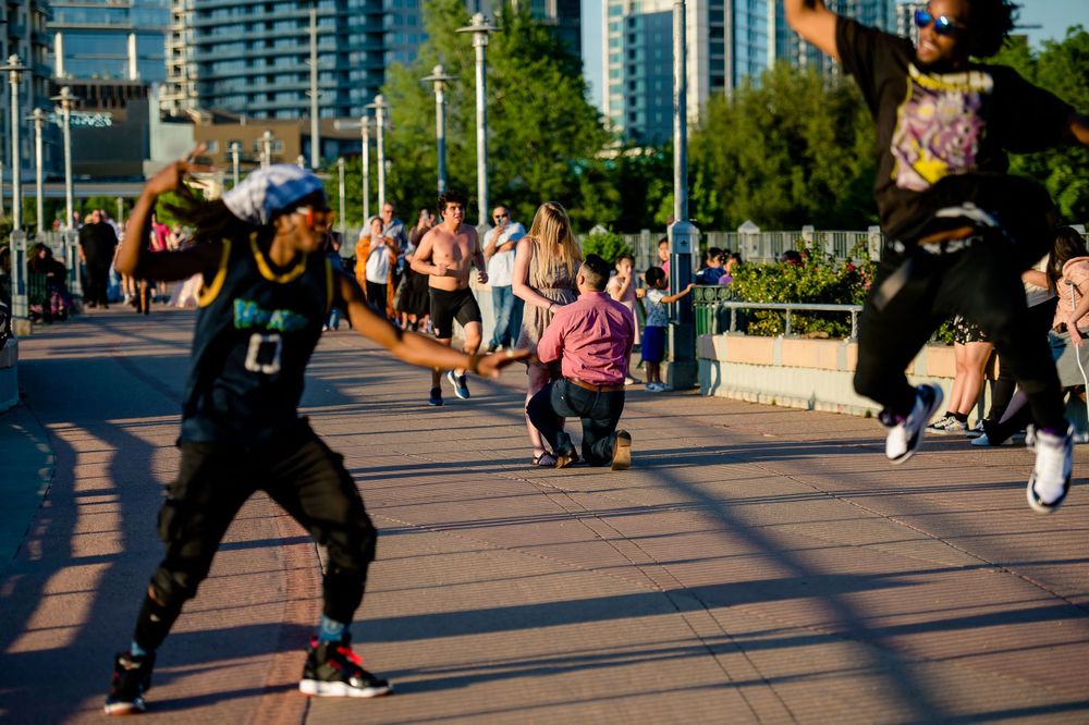Photographers capture a surprise proposal moment on a busy city boardwalk.