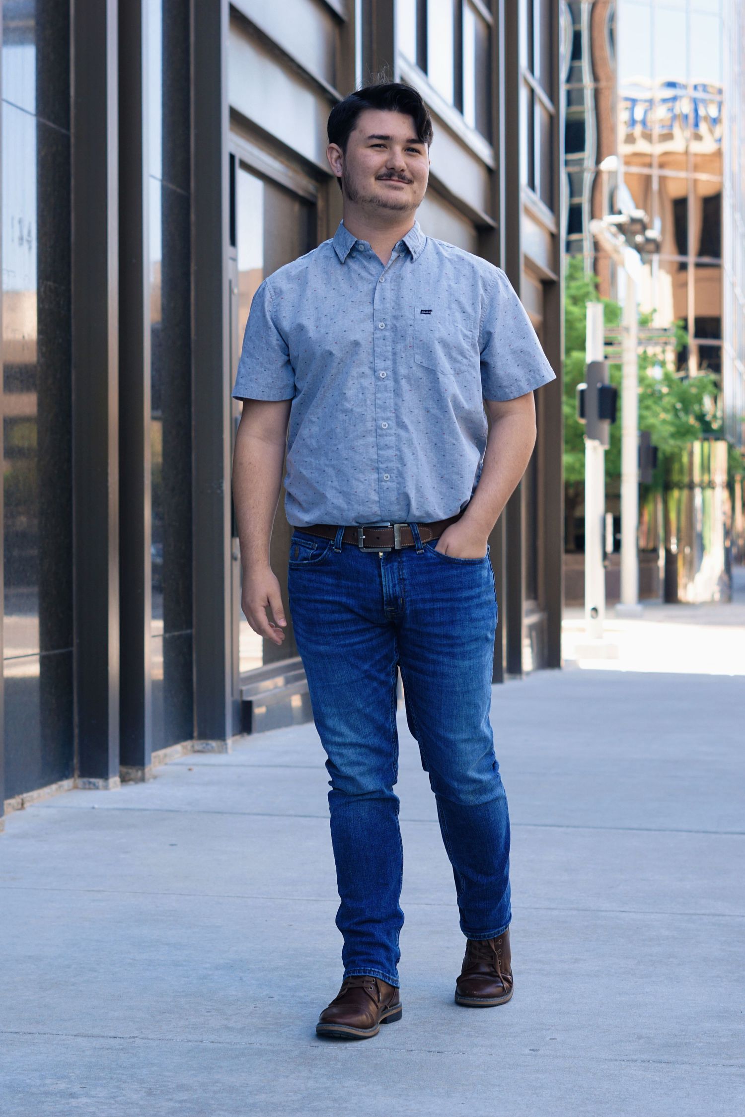 A person in a light blue button-down shirt and jeans stands on an urban sidewalk.