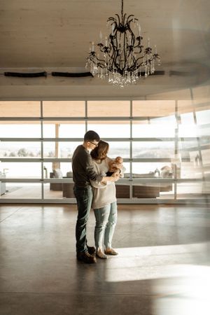 A couple embraces while looking at their phone under an elegant crystal chandelier in a modern space.