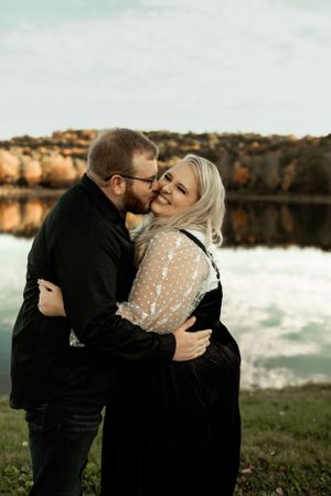 A couple embraces by a reflective lake during golden hour.