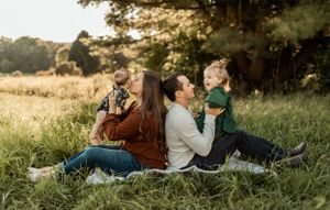 A family sits together in a golden field during sunset sharing a tender moment outdoors.