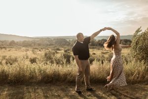 Couple dancing together in golden field at sunset with mountains in background.