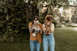 Two people holding up their fluffy dogs while wearing matching denim in outdoor setting.
