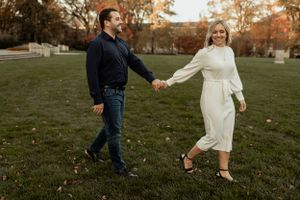 Couple holding hands while walking together on grassy lawn during autumn.