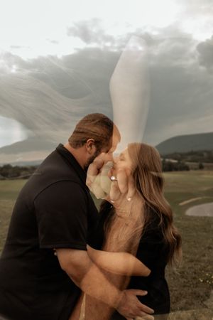Artistic couple's portrait with flowing dress and dramatic clouds in golden hour light.