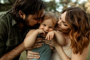 Intimate family moment outdoors with parents embracing laughing child.