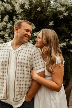 A romantic couple in white outfits sharing a joyful moment against a nature backdrop.