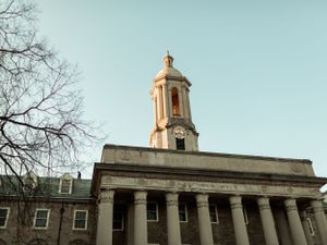 Low angle view of classic collegiate architecture with prominent bell tower against blue sky.