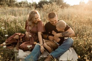 Family sitting together on blanket in sunny meadow during sunset photoshoot.