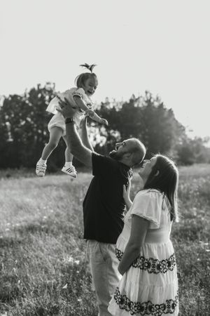Black and white photograph of family playing in sunlit field at sunset.