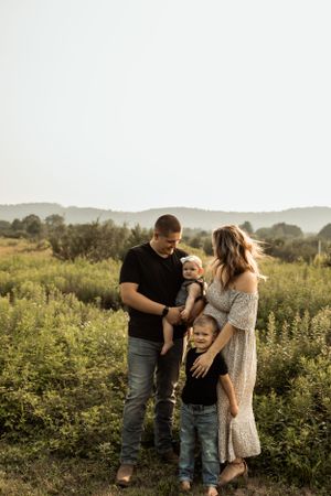 A family stands together in a golden field at sunset holding their small dog.