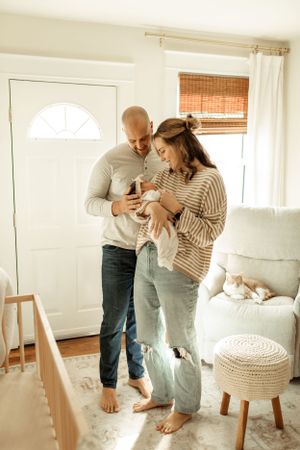 A couple in casual clothing stands barefoot in their bright living room with white decor.