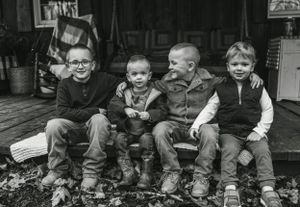 Four children sit side by side on a wooden porch step in black and white.