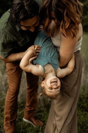 Playful family moment captured outdoors with child being held upside down.