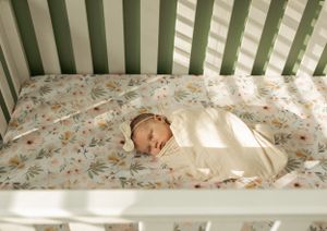 Sleeping newborn in white swaddle lying peacefully in a floral-patterned crib.