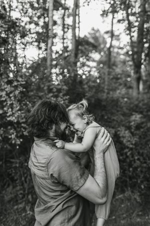 Black and white portrait captures intimate bonding moment between parent and child in forest setting.
