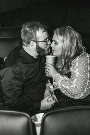 A couple shares a romantic moment while sharing a drink in theater seats.