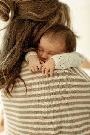 A sleeping baby rests peacefully against a shoulder wearing a striped sweater.