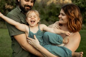 Candid moment of family laughing and playing together in outdoor setting during golden hour.