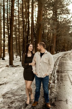 A couple walks together on a snowy forest path wearing casual winter outfits.