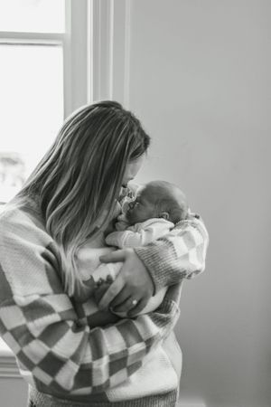 A tender black and white photo of a parent in an argyle sweater holding and gazing lovingly at their newborn baby.