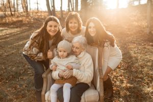 A multigenerational family portrait captured in golden autumn sunlight among trees.