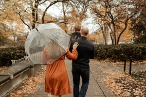 Couple walking with umbrella through fall leaves on rainy autumn day.